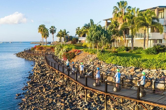 Riders in helmets on the Bicentennial Walkway, a timber boardwalk on the rocks along the Airlie Beach foreshore