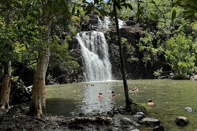 Cedar Creek Falls pouring into its rock-ringed waterhole, swimmers small in the distance