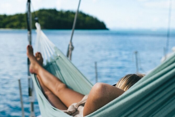 Bare feet up in a hammock slung on a sailing boat, a wooded island across the water