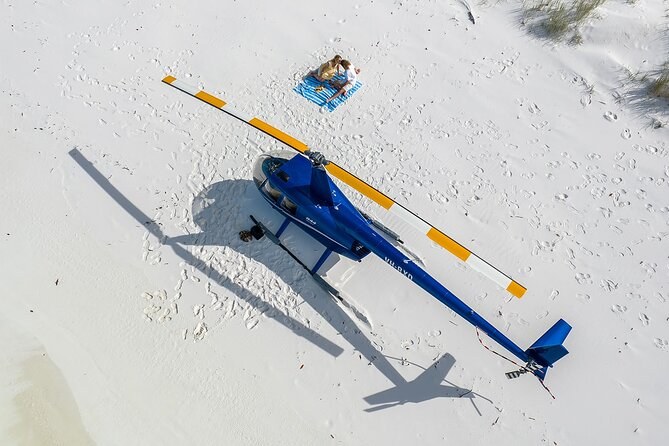 A helicopter parked on white sand, seen from above, a picnic blanket laid out beside it