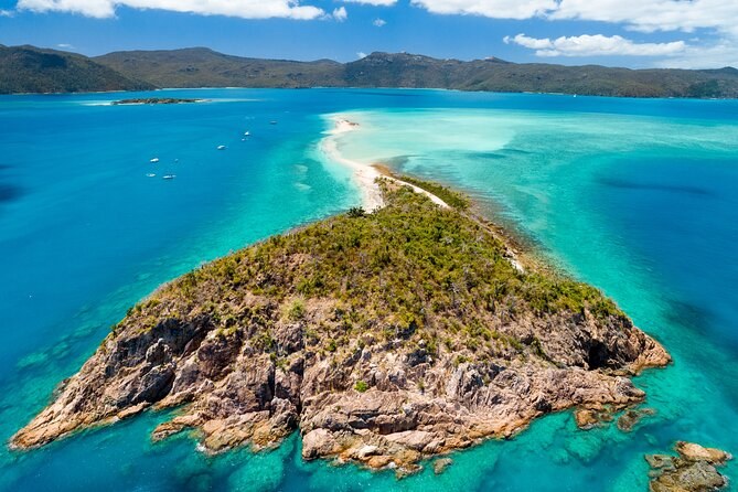 A rocky wooded island trailing a long white sand spit into the turquoise water, seen from the air