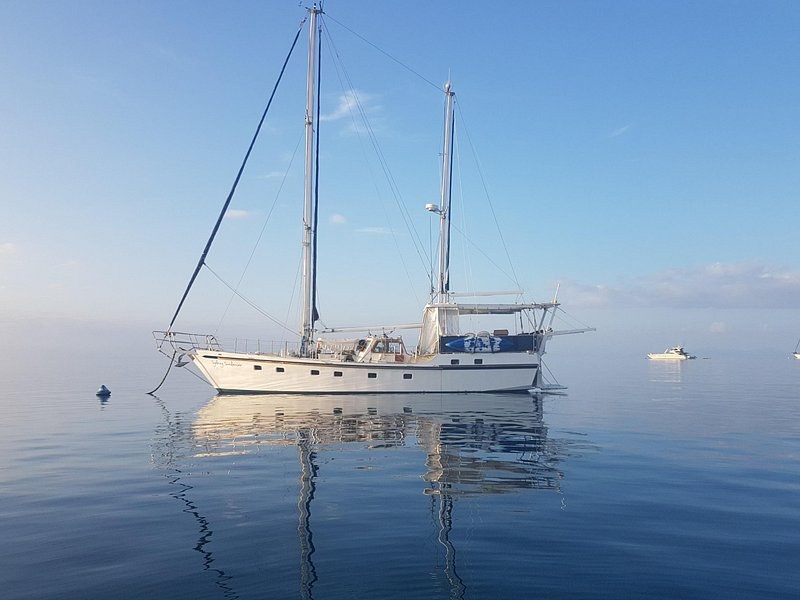 A two-masted yacht at anchor on glassy water in the early light