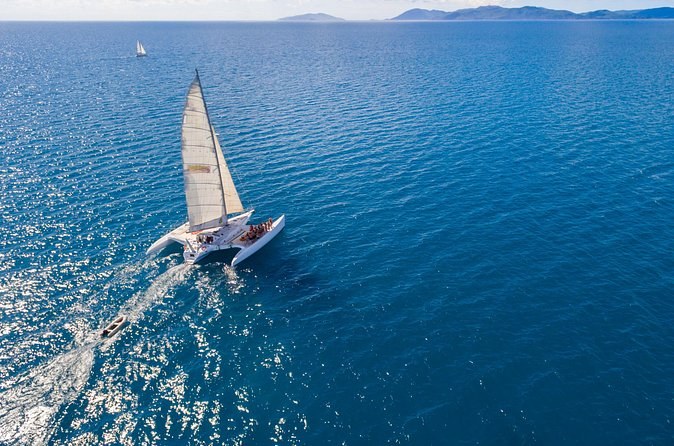 A sailing catamaran under full sail on deep blue water, islands on the horizon
