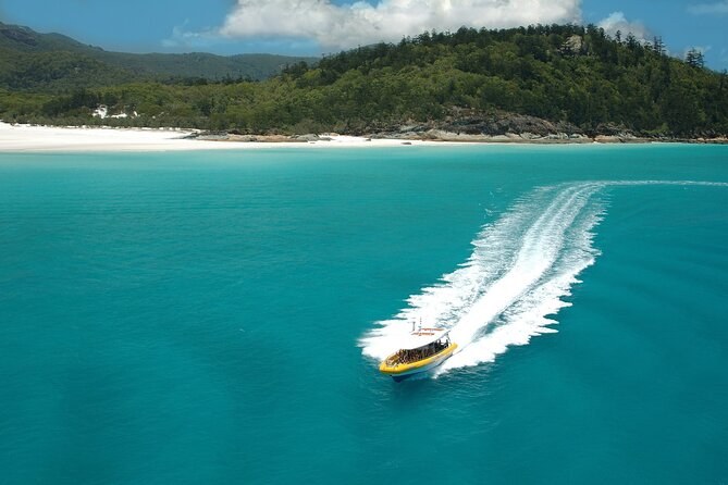 A speedboat drawing a white wake across turquoise water off a long island beach